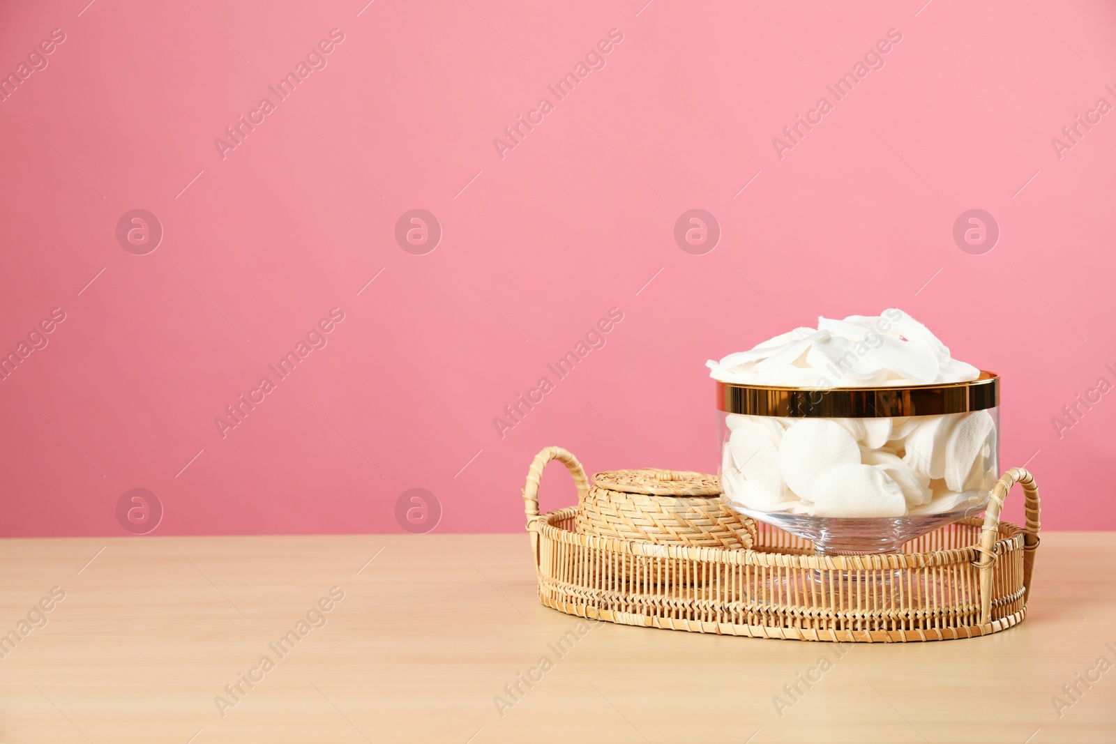 Photo of Jar with cotton pads on wooden table against pink background. Space for text