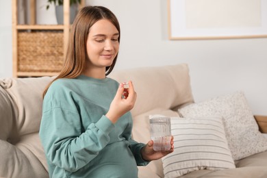 Beautiful pregnant woman holding glass of water and pill at home