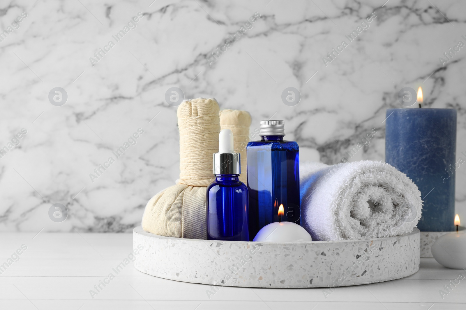 Photo of Spa composition. Bottles of cosmetic products, towel, herbal bags and burning candles on white wooden table, space for text