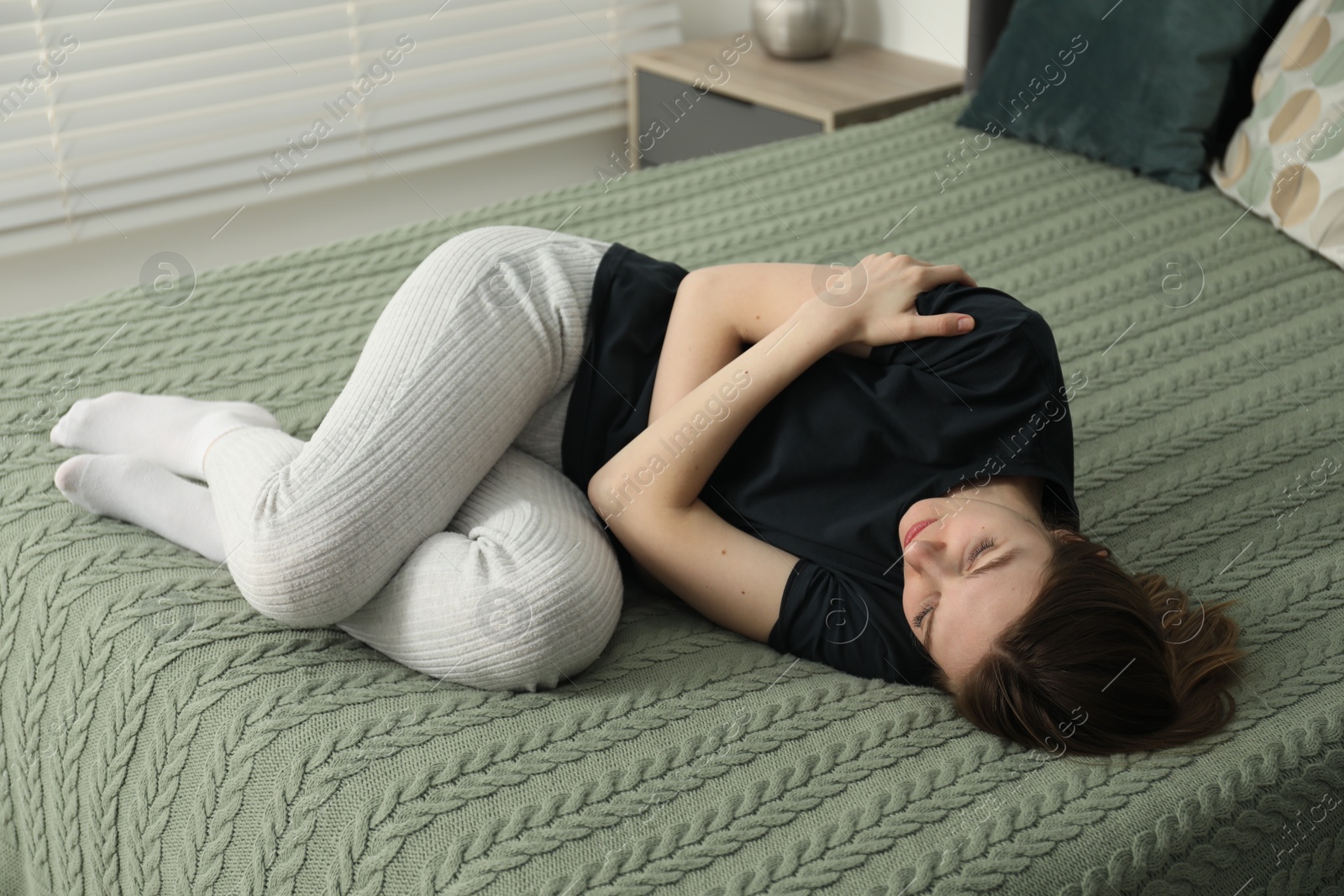 Photo of Sad young woman lying on bed at home