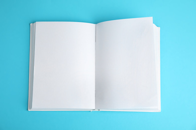 Photo of Open book with blank pages on blue background, top view