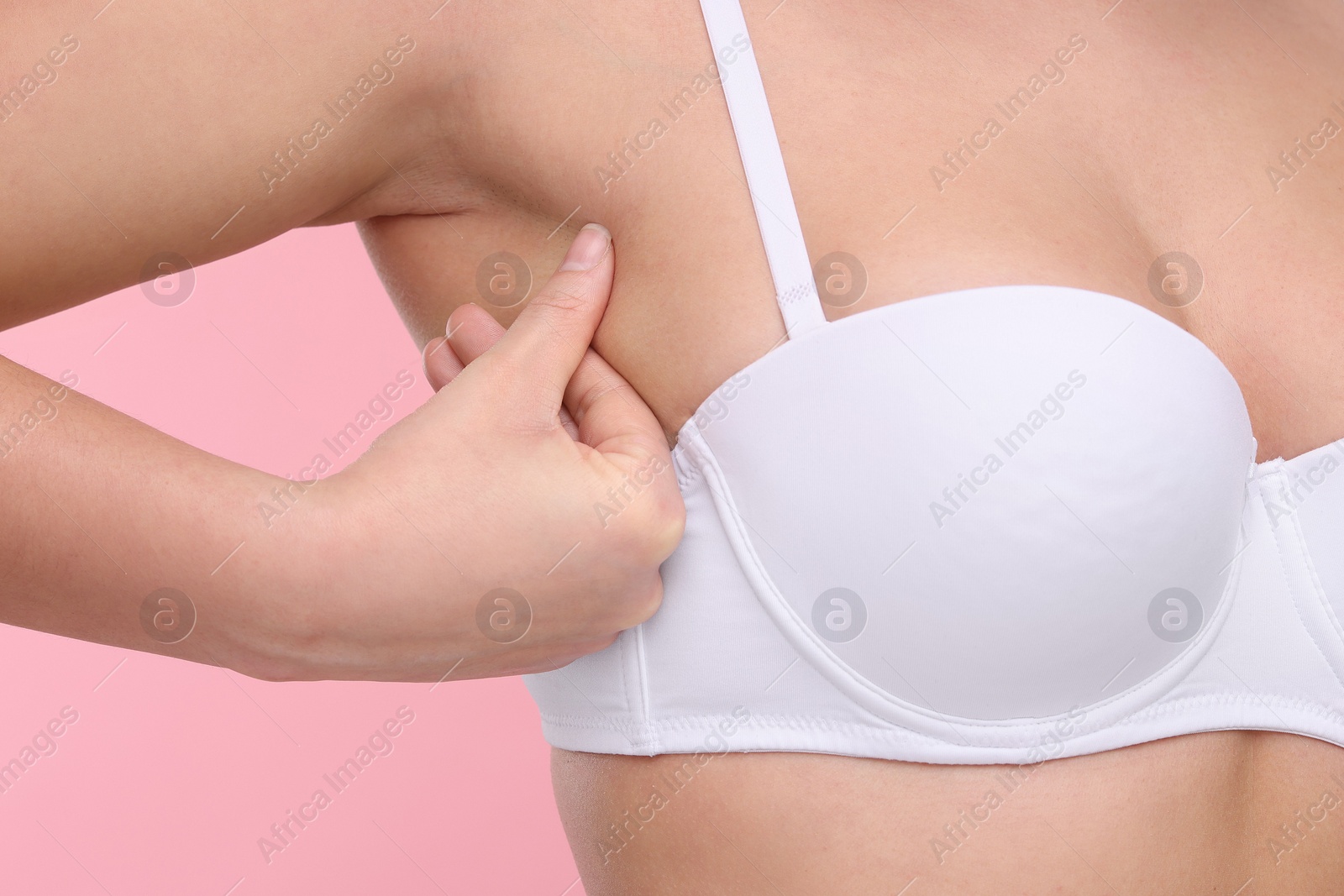 Photo of Mammology. Woman in bra doing breast self-examination on pink background, closeup