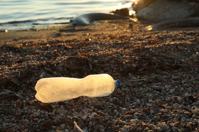 Photo of Used plastic bottle near water at beach, space for text. Environment pollution