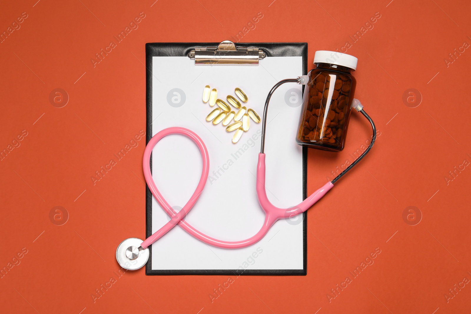 Photo of Stethoscope, pills and clipboard on crimson background, flat lay. Medical tool