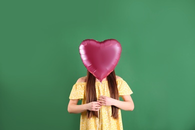 Young woman with heart shaped balloon on color background