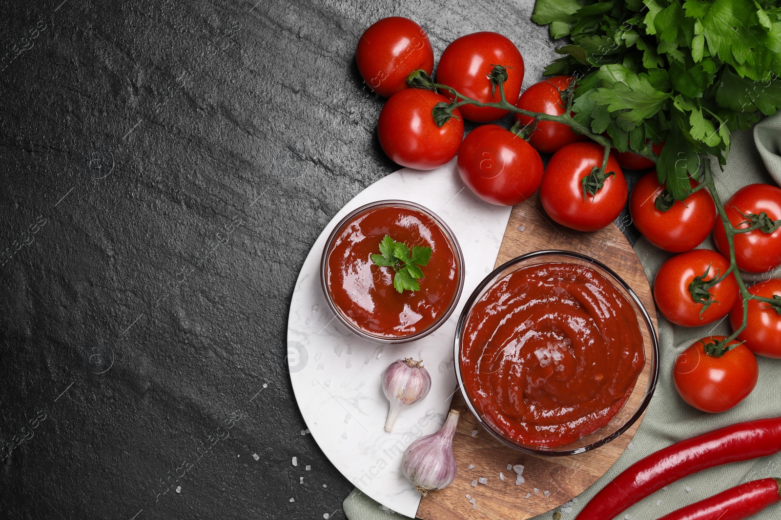 Photo of Organic ketchup in bowls and ingredients on black table, flat lay with space for text. Tomato sauce