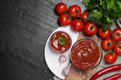 Organic ketchup in bowls and ingredients on black table, flat lay with space for text. Tomato sauce