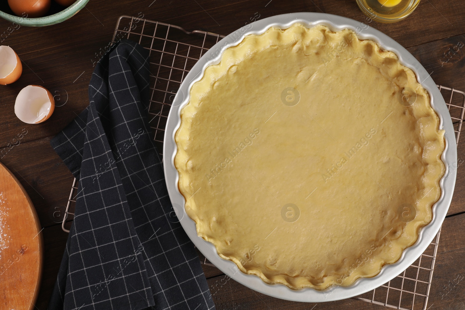 Photo of Pie tin with fresh dough and ingredients on wooden table, flat lay. Making quiche