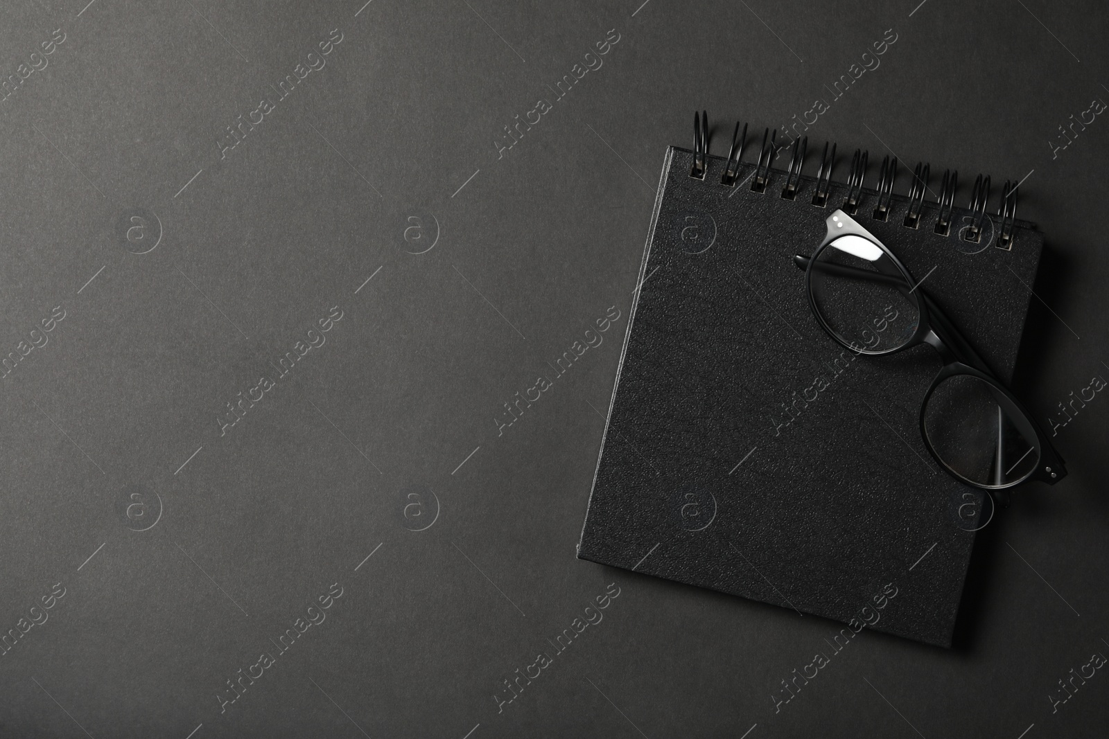 Photo of Glasses, notebook and space for text on dark background, top view. Black Friday concept