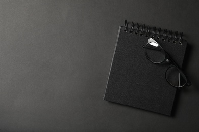 Photo of Glasses, notebook and space for text on dark background, top view. Black Friday concept