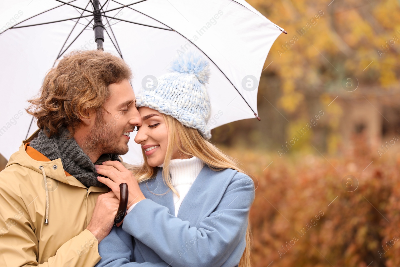 Photo of Young romantic couple with umbrella in park on autumn day