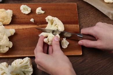 Photo of Woman cutting fresh cauliflower at wooden table, above view
