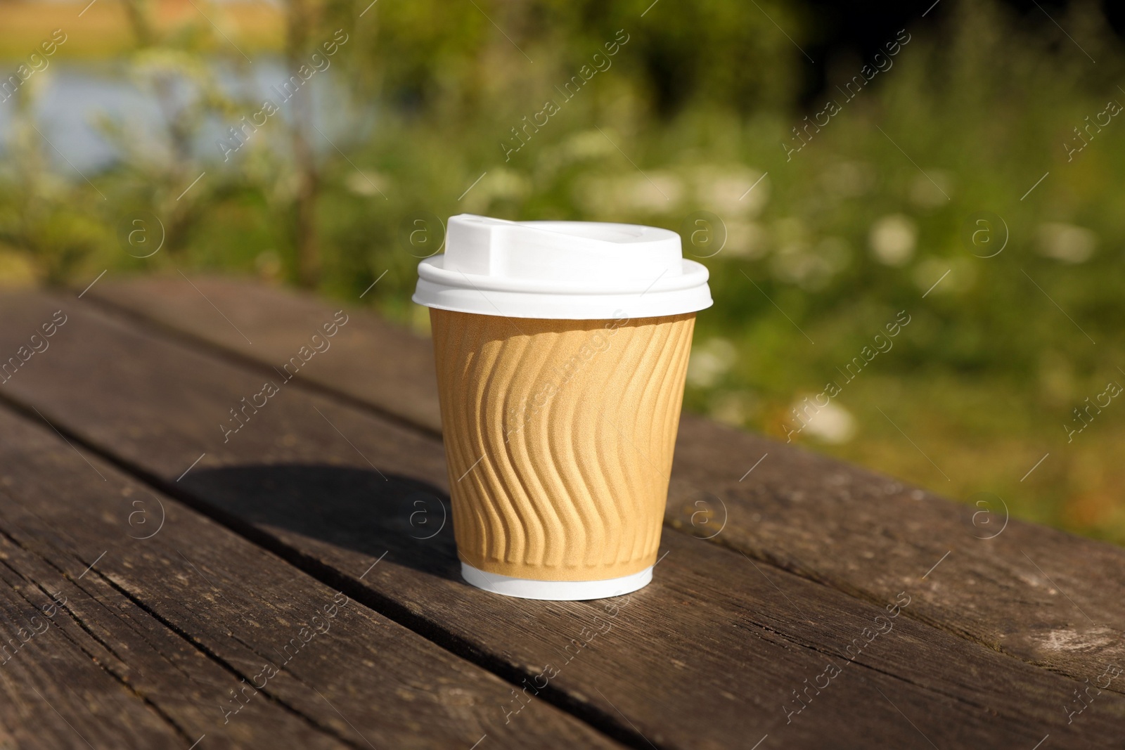 Photo of Paper cup on wooden bench outdoors. Coffee to go