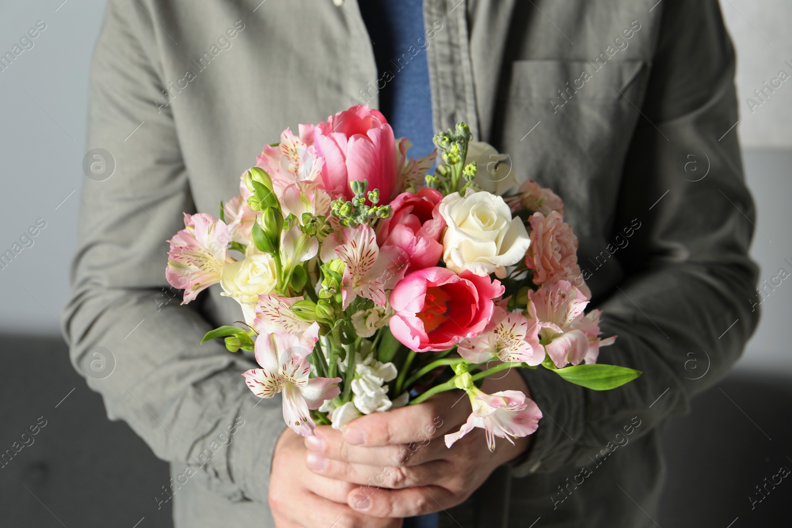 Photo of Man holding bouquet of beautiful flowers indoors, closeup