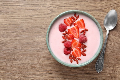 Smoothie bowl with goji berries and spoon on wooden table, flat lay. Space for text