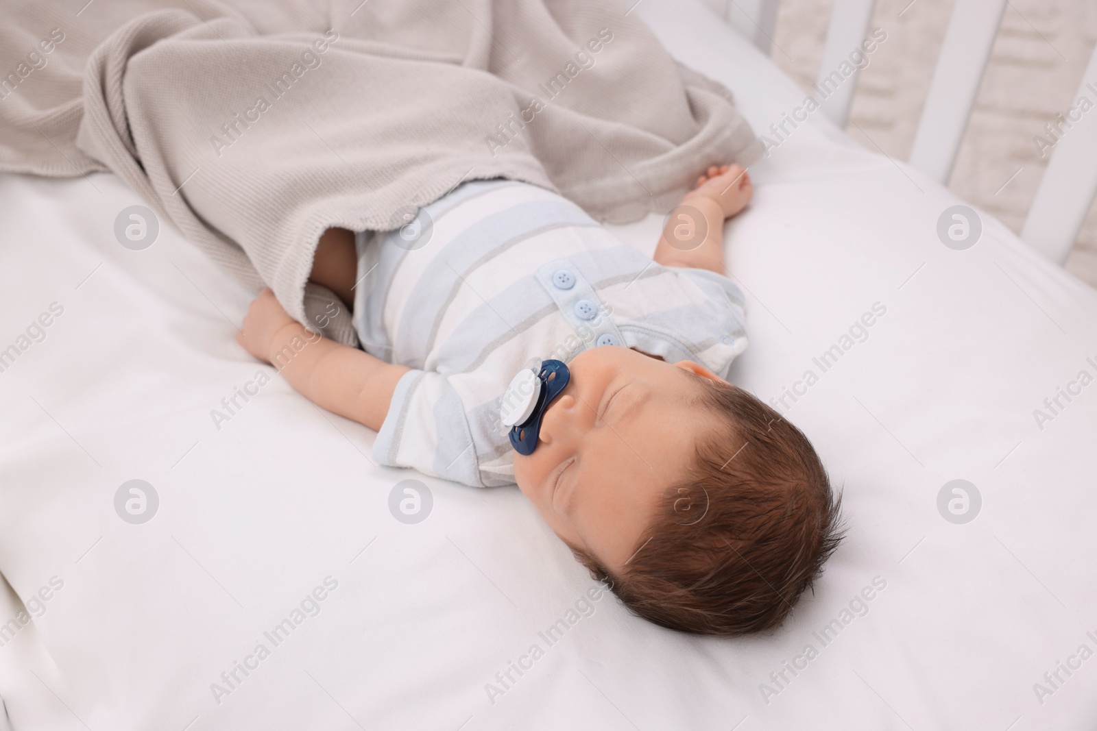 Photo of Cute newborn baby with pacifier sleeping under blanket in crib. Bedtime