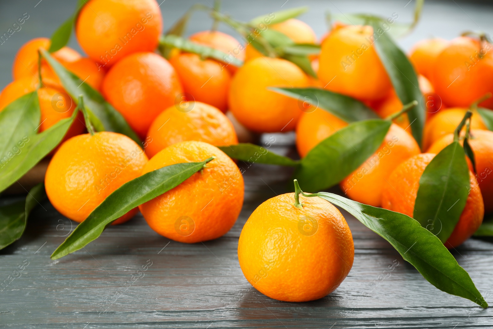 Photo of Fresh ripe tangerines with green leaves on grey wooden table