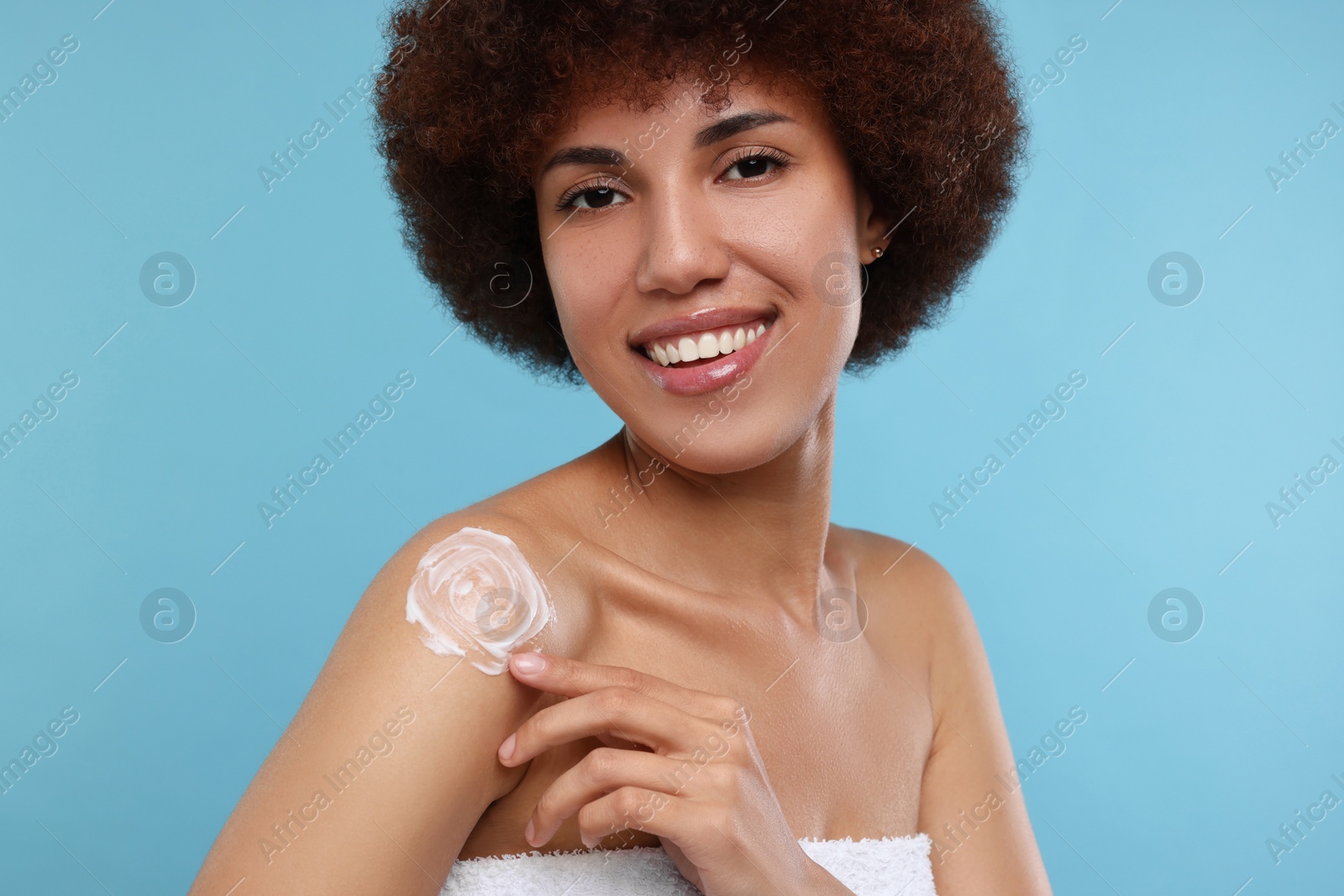 Photo of Beautiful young woman applying body cream onto shoulder on light blue background