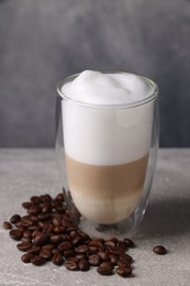 Photo of Aromatic latte macchiato in glass and coffee beans on light grey table