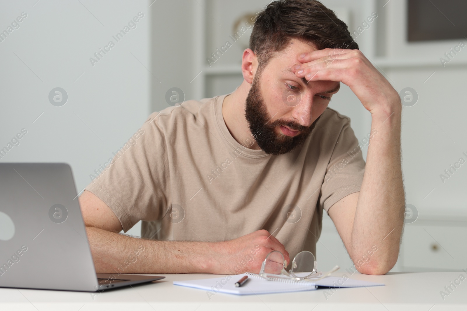 Photo of Overwhelmed man sitting with laptop at table indoors