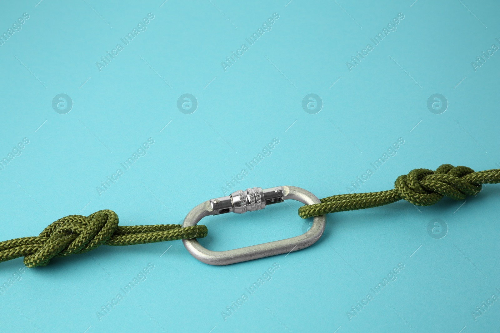 Photo of One metal carabiner with ropes on light blue background. Space for text