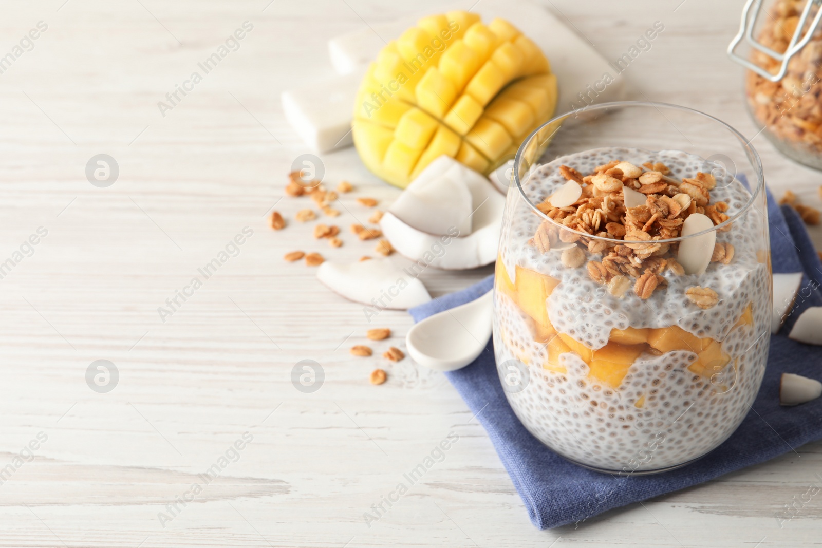 Photo of Delicious chia pudding with granola and mango on white wooden table, space for text