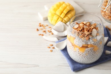 Delicious chia pudding with granola and mango on white wooden table, space for text