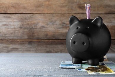 Image of Black piggy bank with money on wooden table, space for text