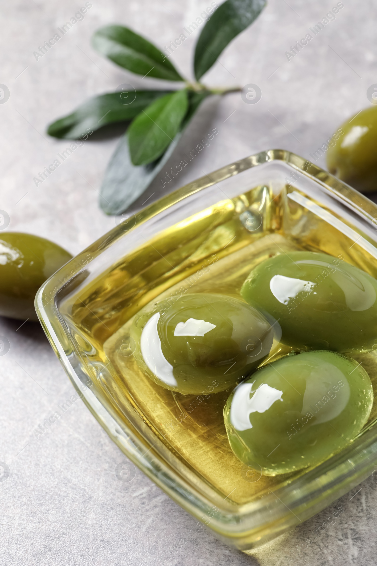 Photo of Glass bowl with fresh olive oil on light grey table, closeup