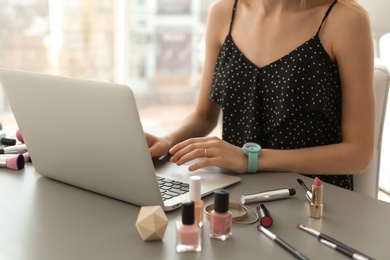 Photo of Young woman with makeup products using laptop at table. Beauty blogger