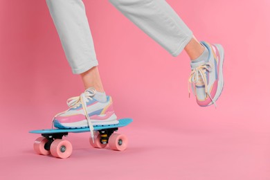 Woman in new stylish sneakers standing on skateboard against pink background, closeup