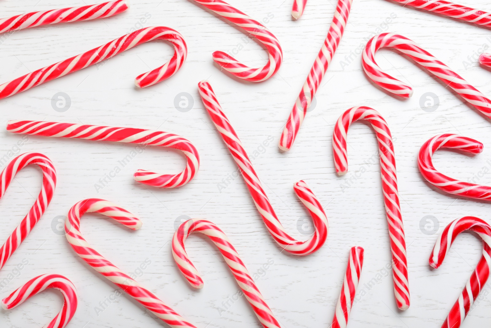 Photo of Sweet Christmas candy canes on white wooden 
background, flat lay