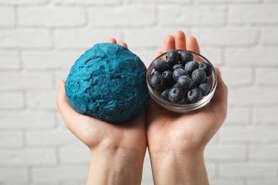 Photo of Woman holding dough painted with natural food coloring and blueberries white brick wall, closeup