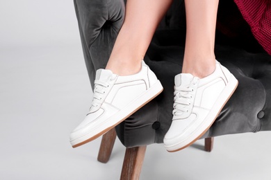 Photo of Woman with stylish sport shoes sitting in armchair on light background