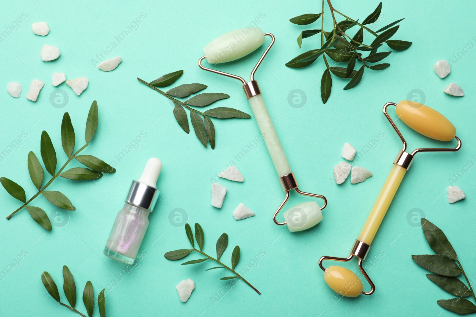 Photo of Natural face rollers, cosmetic product and leaves on turquoise background, flat lay