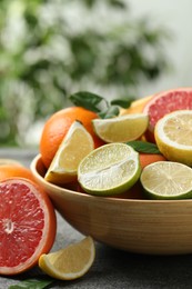 Photo of Different fresh citrus fruits and leaves on table against blurred background, closeup
