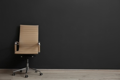 Photo of Comfortable office chair near black wall indoors. Space for text