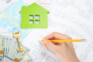 Cartographer with key, house model and money drawing cadastral map, closeup