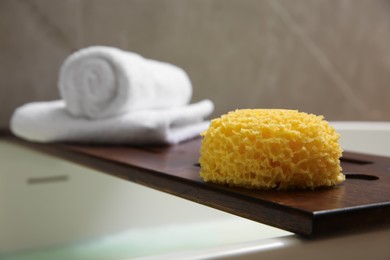 Photo of Wooden bath tray with sponges and towel on tub, closeup