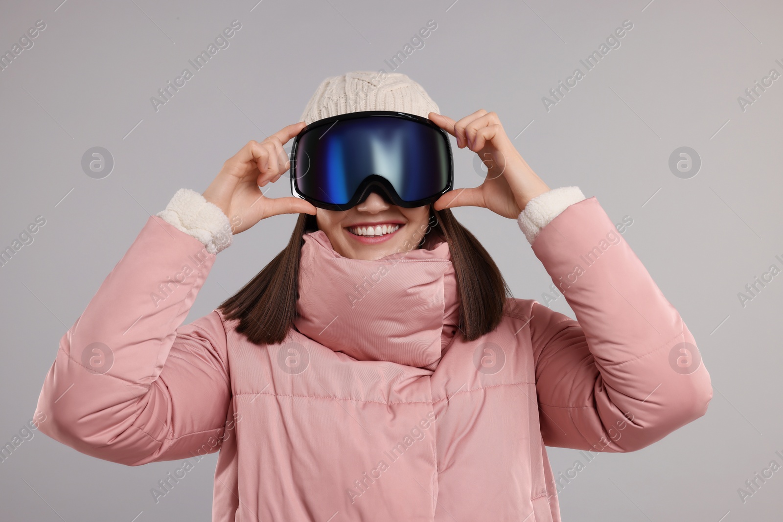 Photo of Winter sports. Happy woman with snowboard goggles on grey background