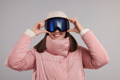 Winter sports. Happy woman with snowboard goggles on grey background