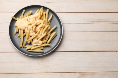 Photo of Delicious french fries with cheese sauce on wooden table, top view. Space for text