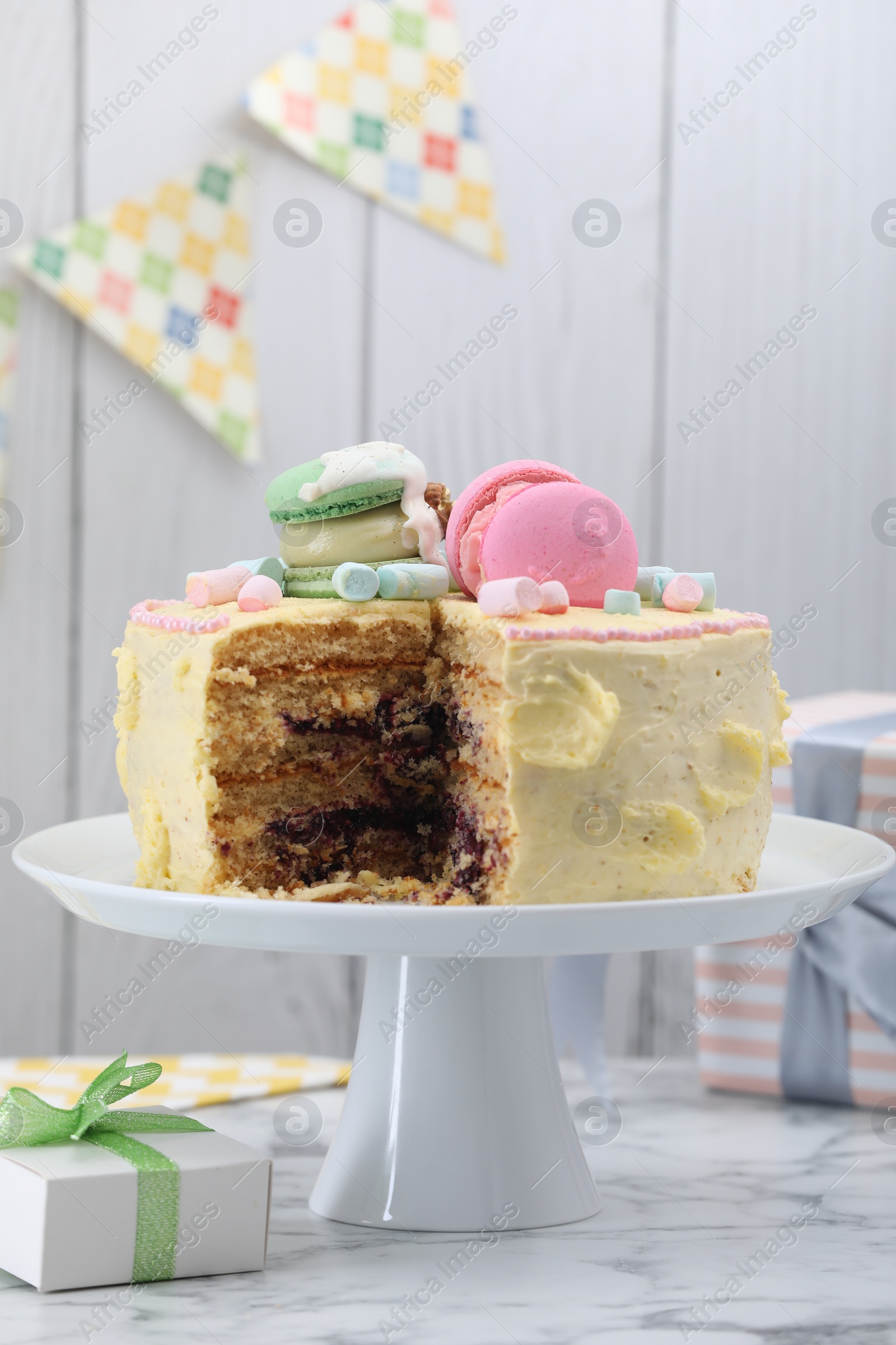 Photo of Delicious cake decorated with macarons and marshmallows and gift box on white marble table