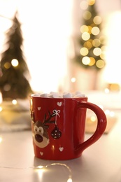 Photo of Hot drink with marshmallow and festive lights on table indoors