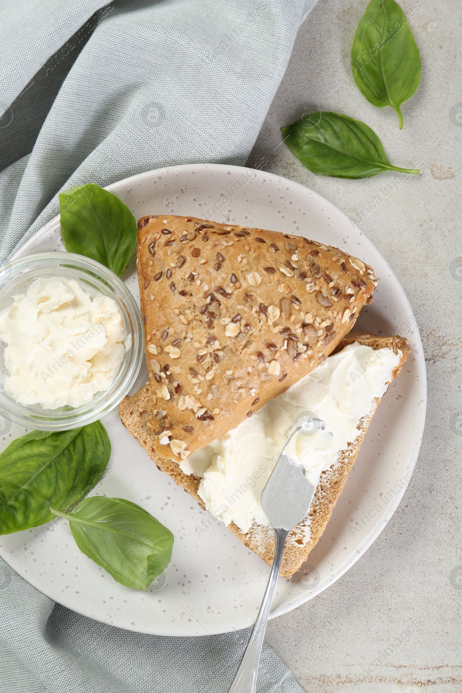 Photo of Pieces of bread with cream cheese and basil leaves on light gray table, top view