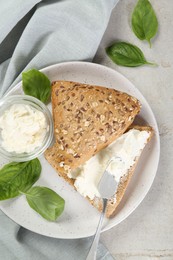 Pieces of bread with cream cheese and basil leaves on light gray table, top view