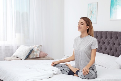 Young beautiful woman meditating on bed at home. Morning fitness