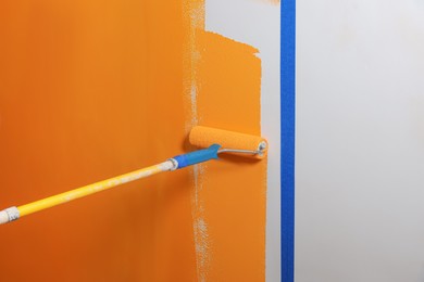 Person painting wall with roller and orange dye