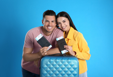 Photo of Happy couple with suitcase and tickets in passports for summer trip on blue background. Vacation travel