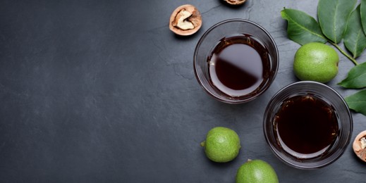 Image of Delicious liqueur and fresh walnuts on black table, flat lay with space for text. Banner design